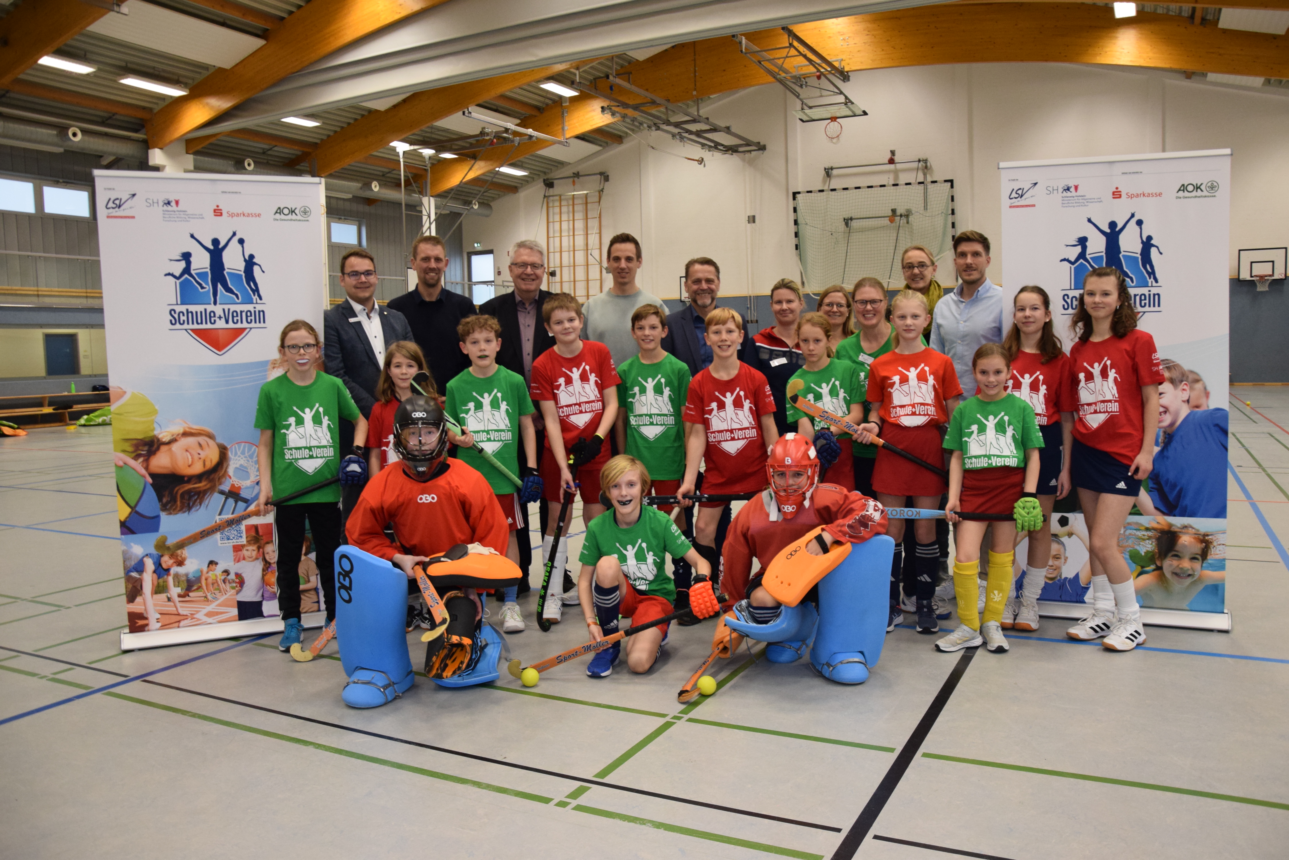 Schülerinnen und Schüler (5.-8. Klassen) der Johannes-Brahms-Schule in Pinneberg freuen sich über das außerunterrichtliche Hockey-Angebot, das der VfL Pinneberg als Kooperationspartner im Rahmen des LSV-Projekts &quot;Schule+Verein&quot; an der Schule anbietet. Hier gemeinsam mit Vertreterinnen und Vertretern von Schule, Verein, AOK Nordwest, Sparkasse Südholstein sowie Kreissportverband Pinneberg und Landessportverband Schleswig-Holstein. - Foto: LSV/Stefan Arlt